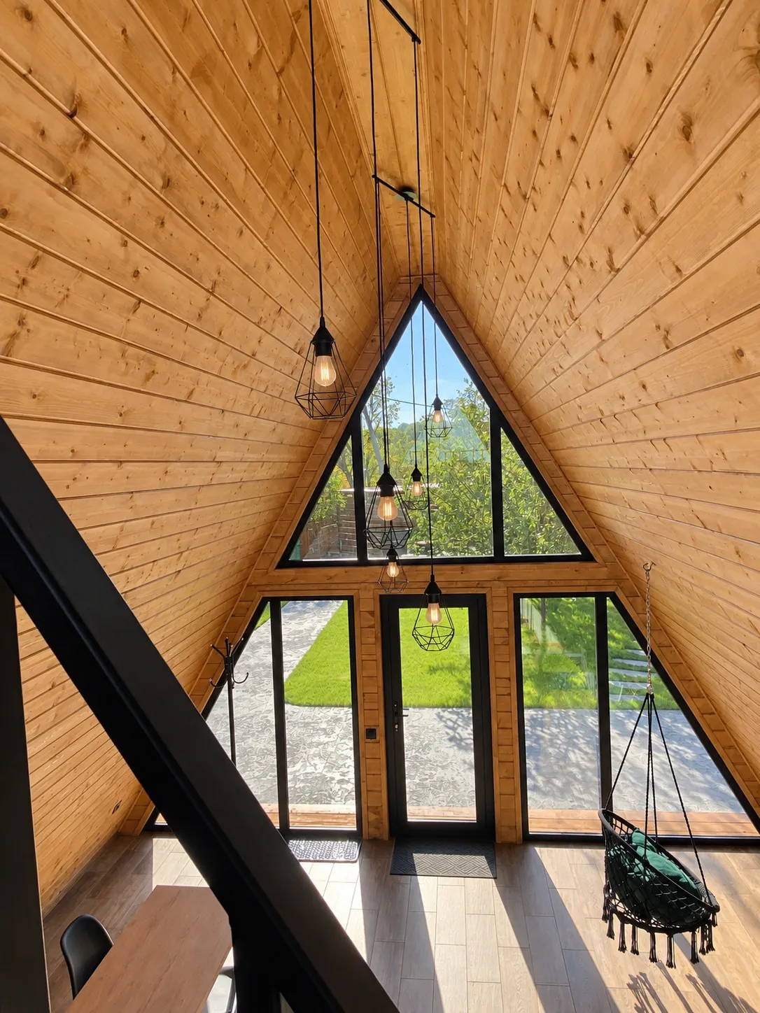 Гостиная A-frame дома: деревянный потолок, стеклянный фасад и подвесное кресло